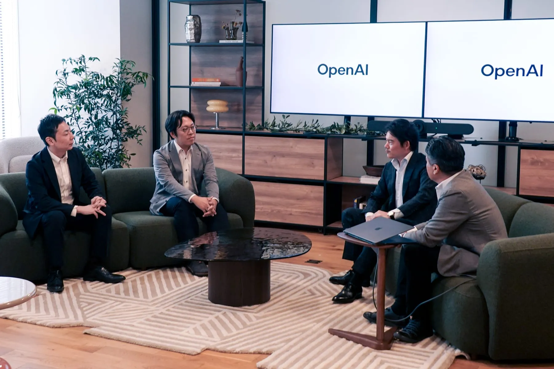 OpenAI Japan のオフィスで開かれたメディア向け座談会。ソファに向かい合って座る4名が議論しており、背景には OpenAI のロゴを表示した2台のディスプレイが並んでいる