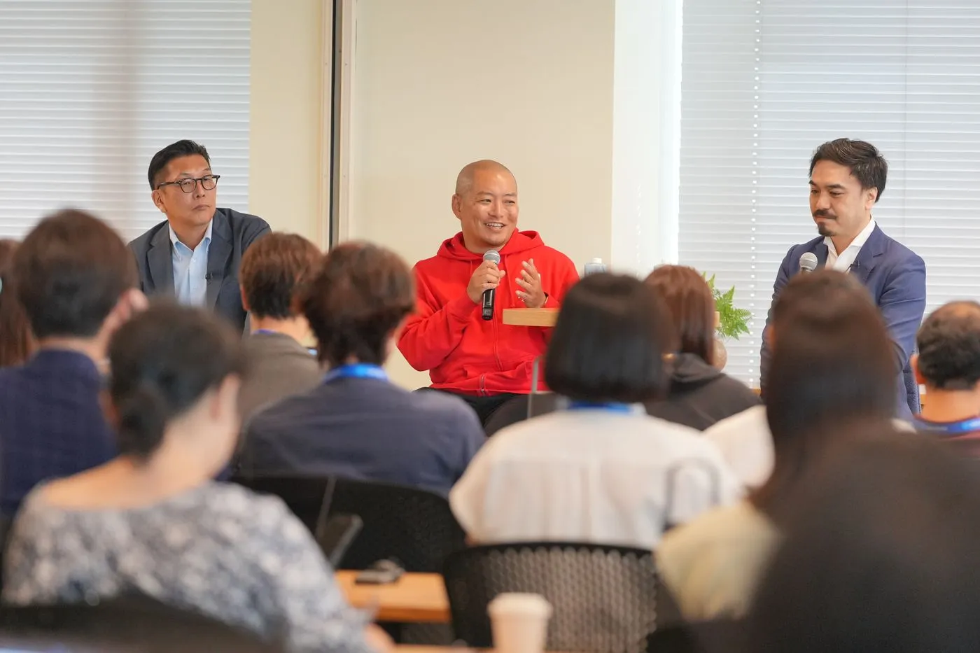 Marketing & Commerce Innovation Day の基調講演パネルディスカッションで、赤いフーディーを着てマイクを持ち話す株式会社リバネスナレッジ取締役副社長 平塚武。左に株式会社かんぽ生命保険の中根祐二氏、右に株式会社セールスフォース・ジャパンの島田崇史氏が並び、満席の会場が聞き入っている